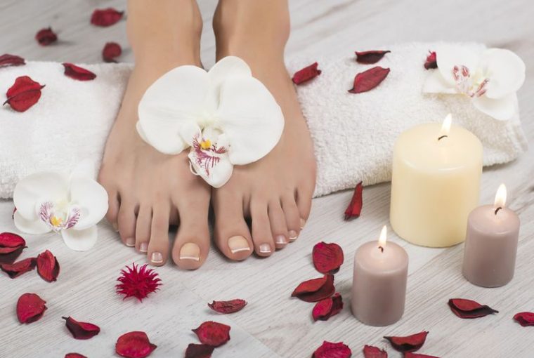 Schöne Füße mit french Maniküre auf weißen Handtuch. Orchidee blüht, roten Blüten und Kerzen um hölzerne Hintergrund. Spa, Fußpflege